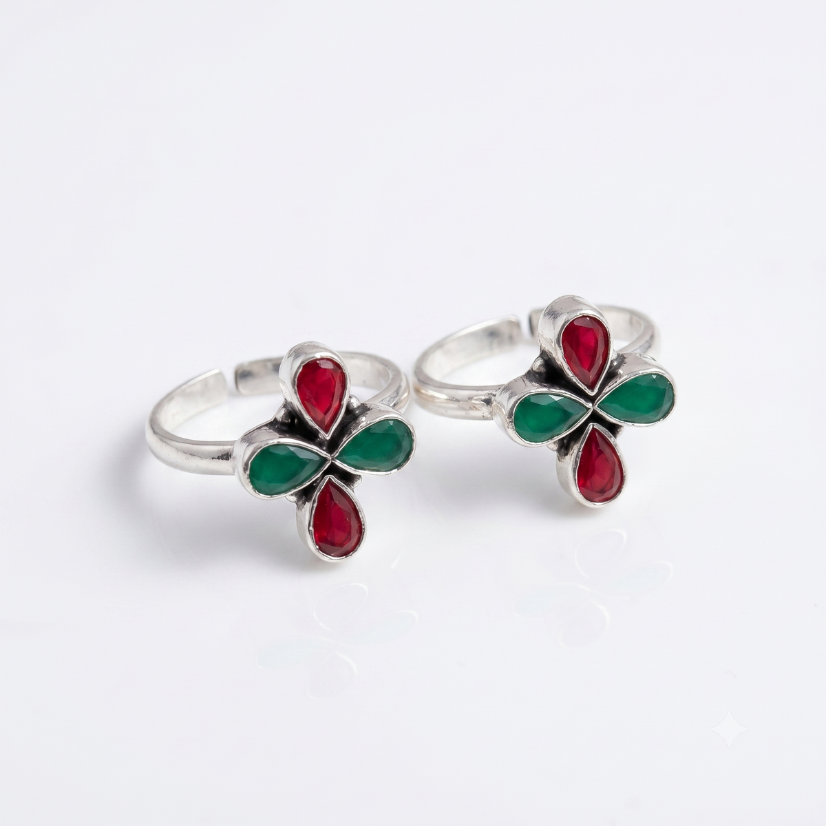 A pair of silver toe rings featuring a four-petal flower design with red and green enamel details