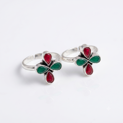 A pair of silver toe rings featuring a four-petal flower design with red and green enamel details