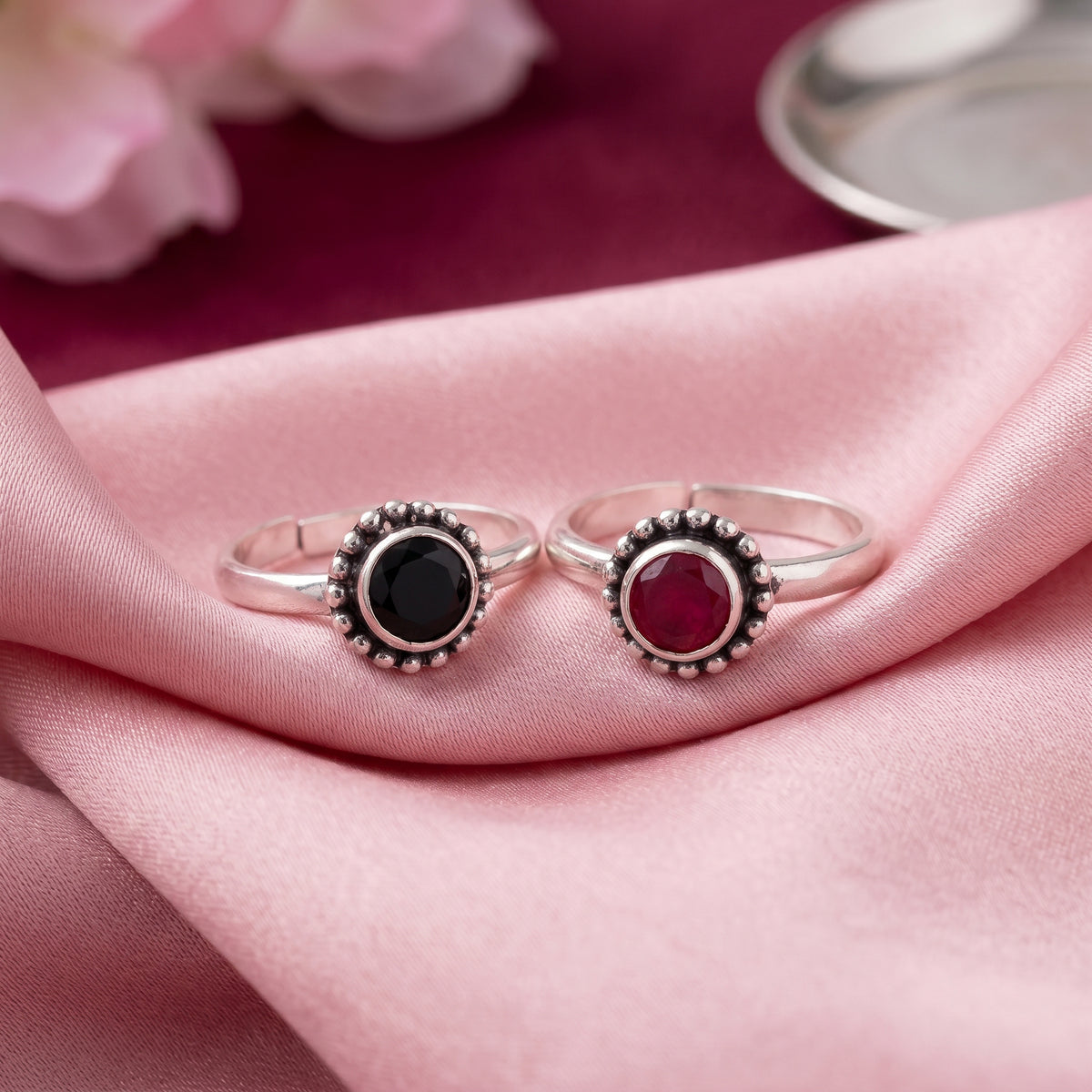 Two silver toe rings with round bezel-set gemstones, one green and one red